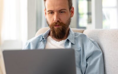 Young Bearded Man Sitting On Sofa At Home Using Laptop Computer